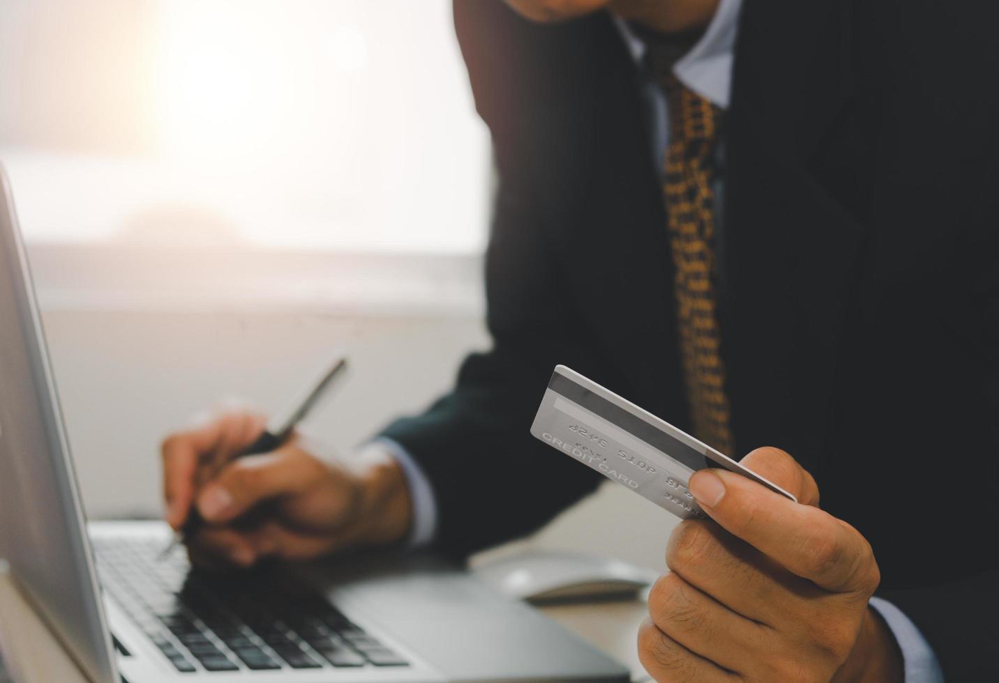 hombre sosteniendo una tarjeta de crédito y trabajando en la computadora portátil foto