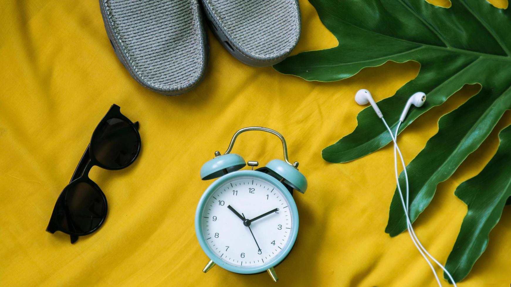 Reloj despertador, auriculares portátiles de hoja sobre un fondo amarillo brillante foto