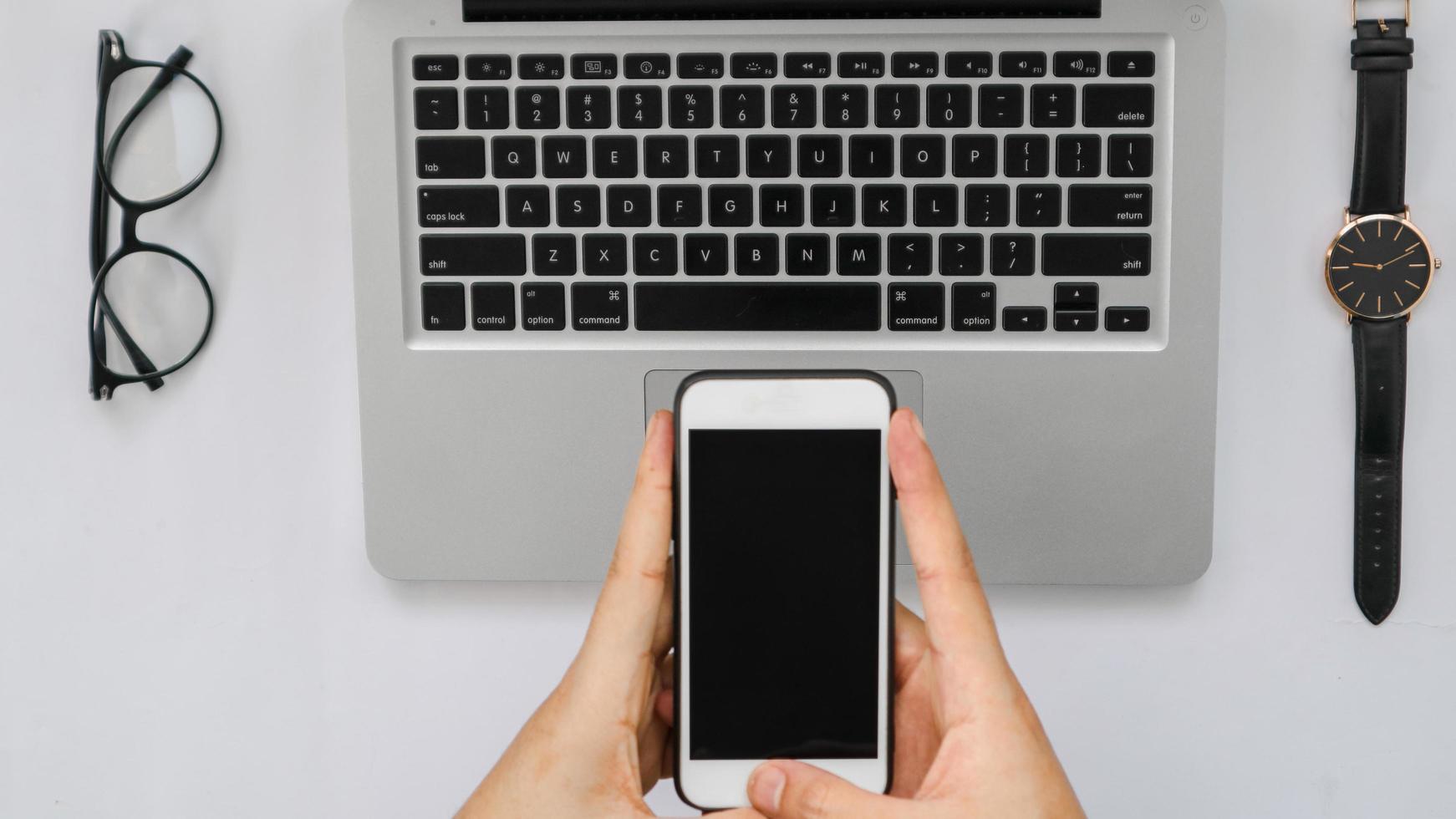 Smartphone over laptop, tablet pen, glasses and watch on white photo