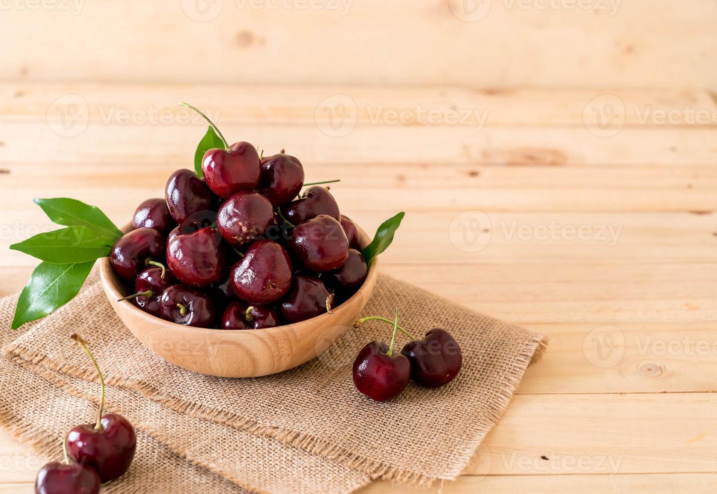 Cereza fresca en tazón de madera sobre la mesa foto