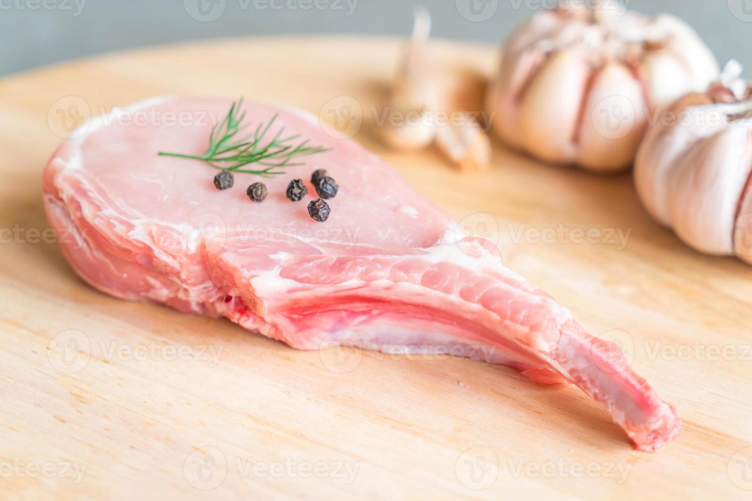 Chuleta de cerdo fresca sobre tablero de madera con ajo y pimientos negros foto