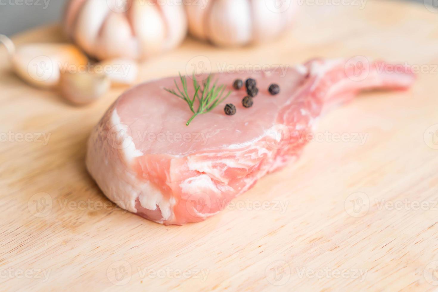 Chuleta de cerdo fresca sobre tablero de madera con ajo y pimientos negros foto