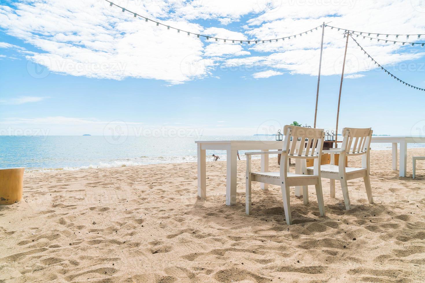 Mesa y sillas blancas en la playa con vistas al mar azul y al cielo despejado foto