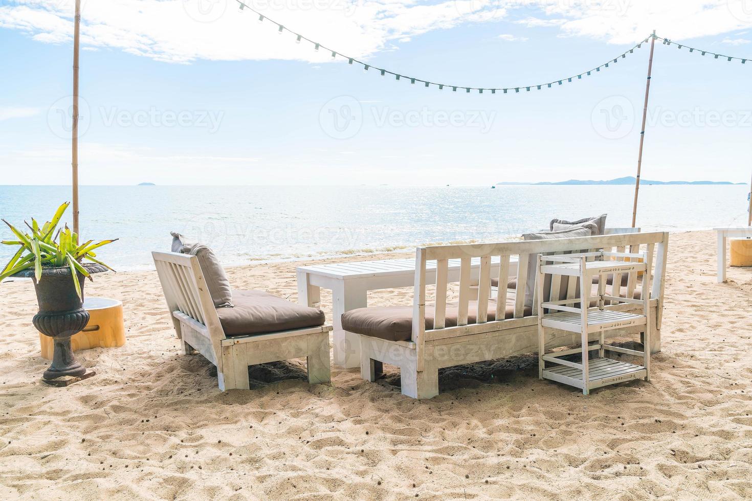 Mesa y sillas blancas en la playa con vistas al mar azul y al cielo despejado foto