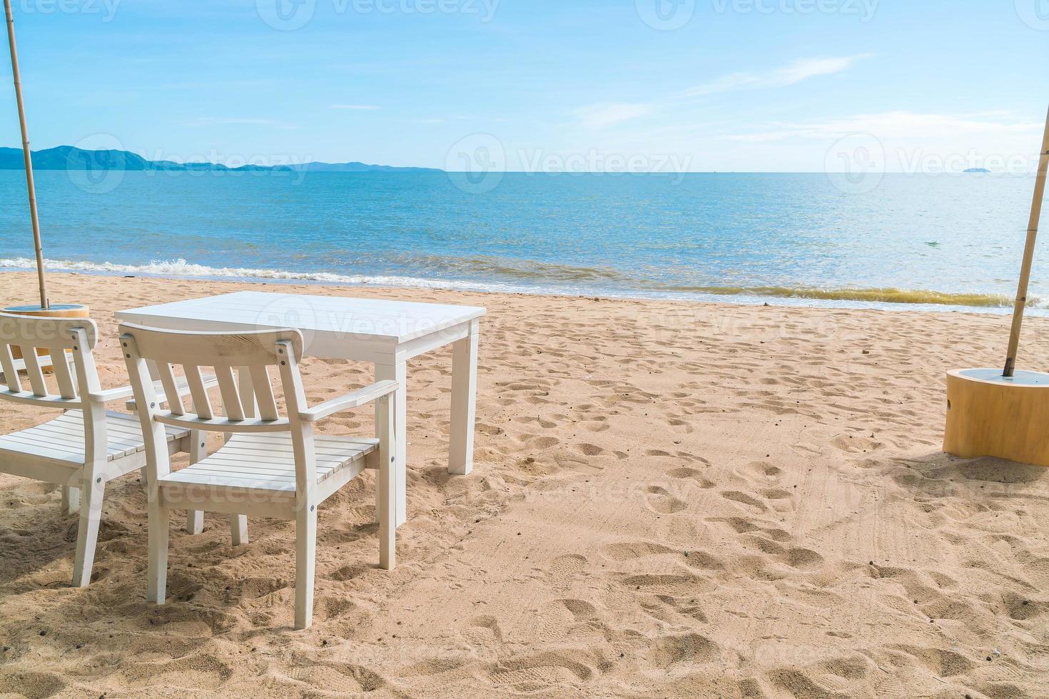 Mesa y sillas blancas en la playa con vistas al mar azul y al cielo despejado foto