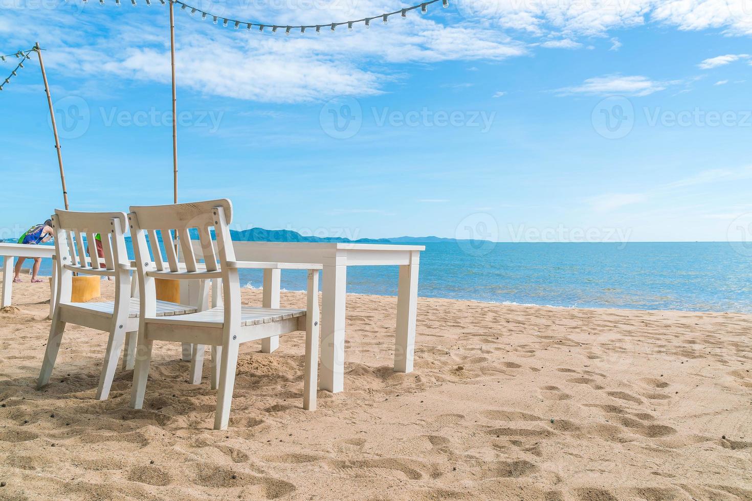 Mesa y sillas blancas en la playa con vistas al mar azul y al cielo despejado foto