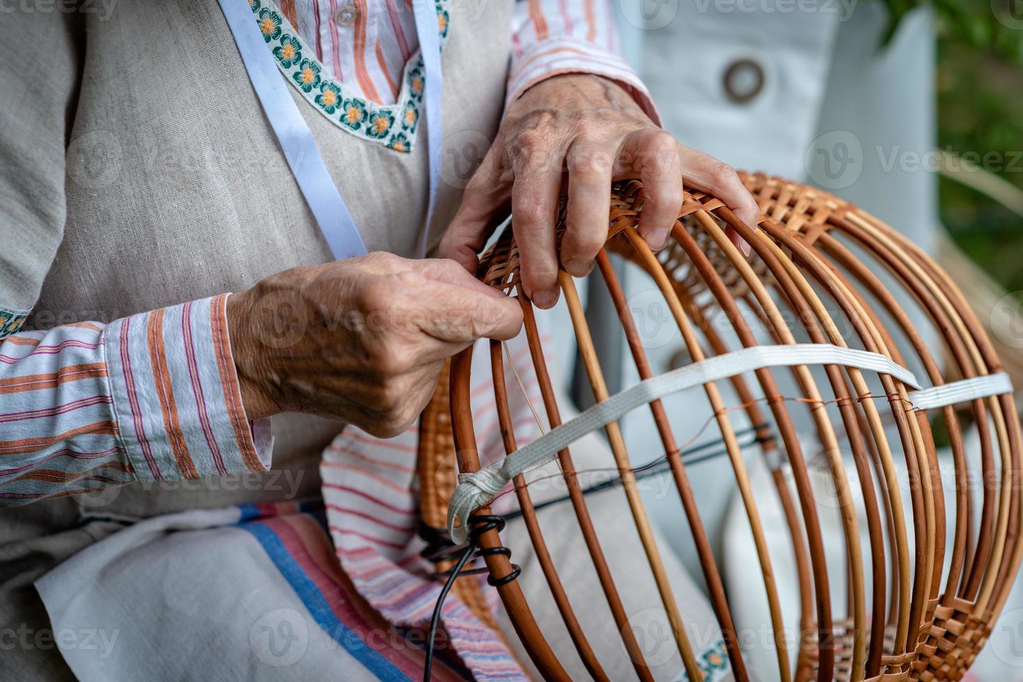 Old woman in national costume make local wicker basket. photo