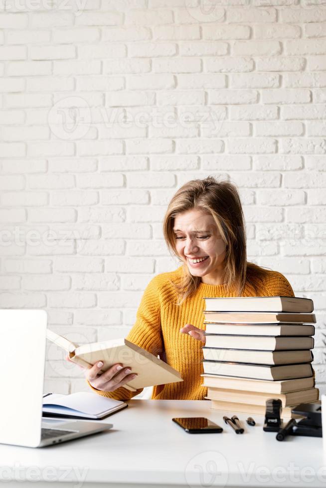 Joven mujer sonriente en suéter amarillo leyendo un libro y riendo foto