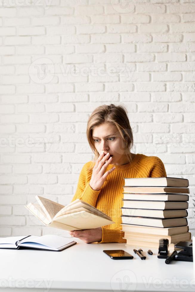 Young smiling woman in yellow sweater reading a book looking surprised photo