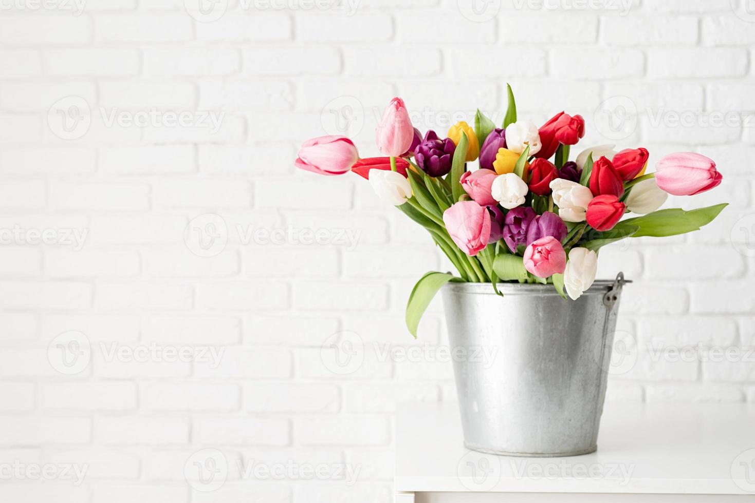 Balde de flores de tulipán sobre fondo de pared de ladrillo blanco foto