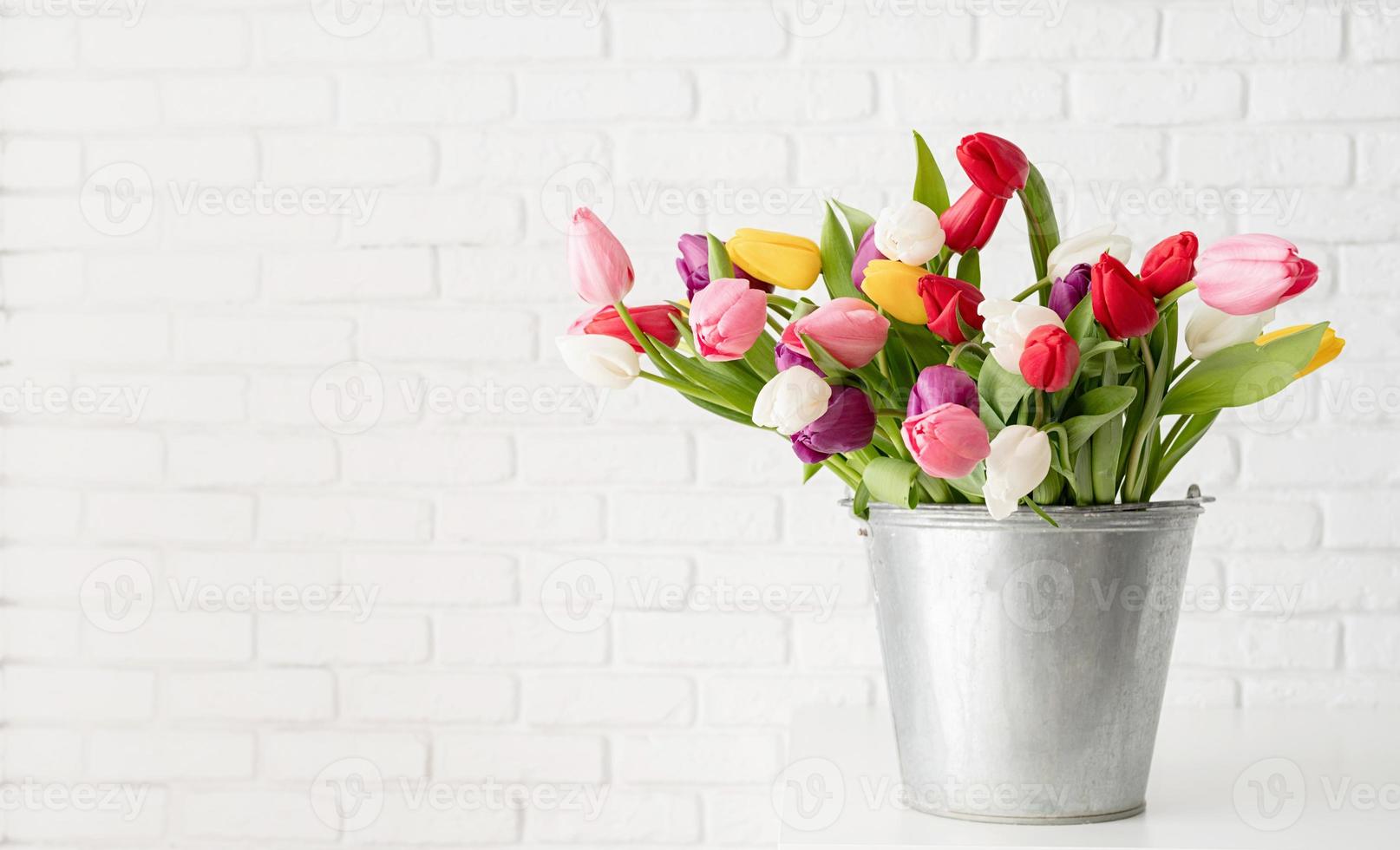 Bucket of tulip flowers over white brick wall background photo