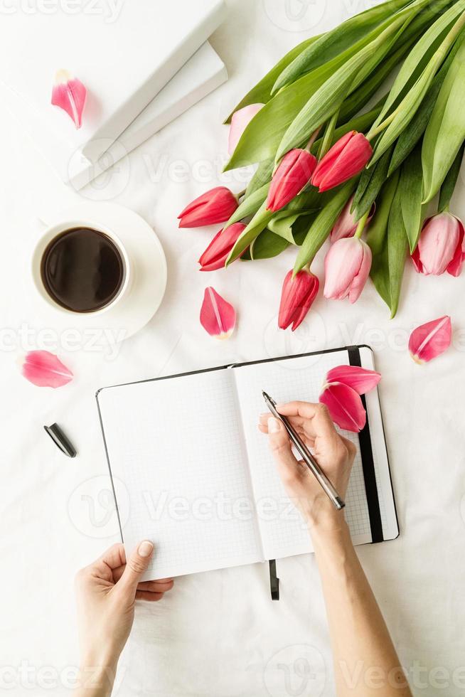 woman hands writing in notebook with tulips on white bed photo