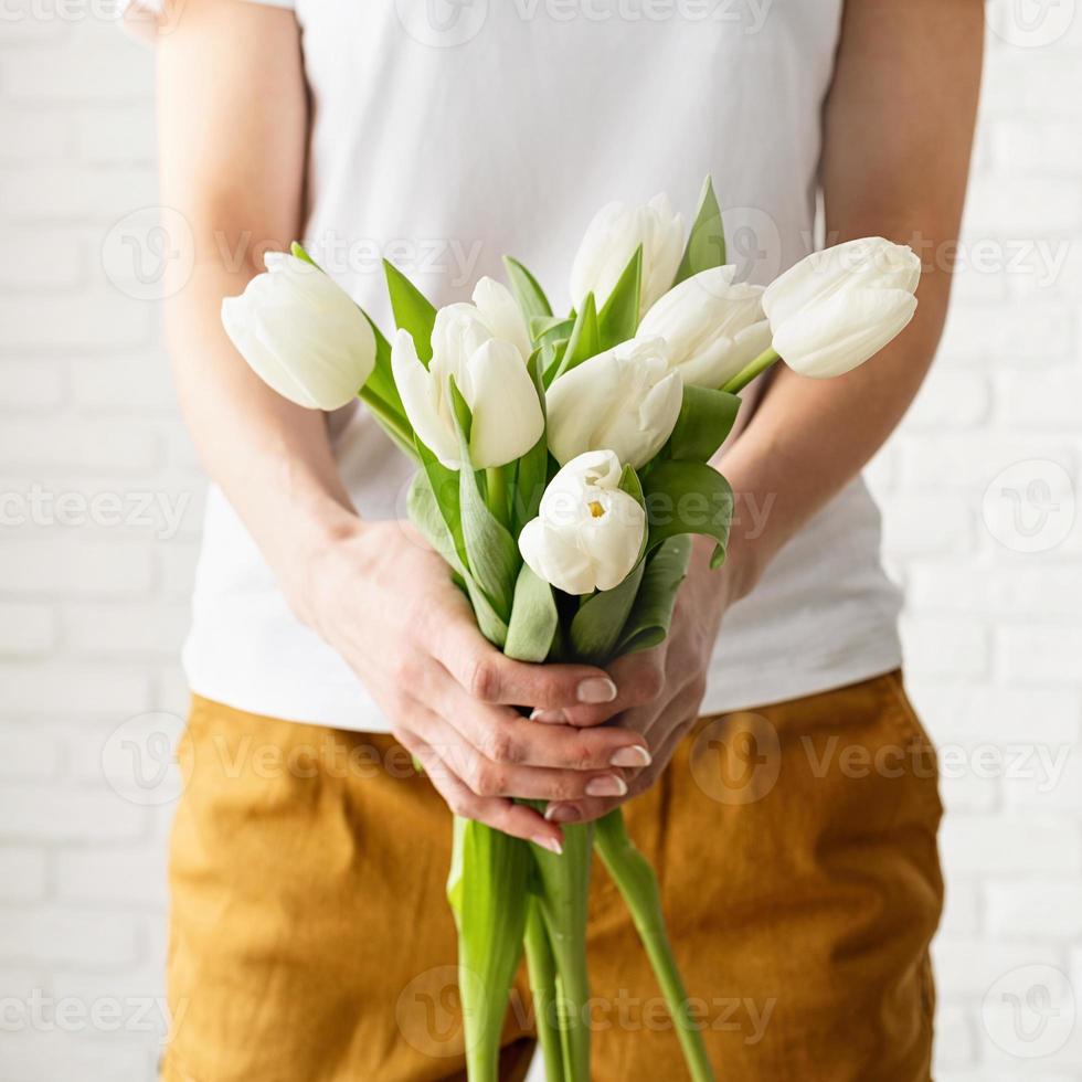 woman in yellow clothes holding bouquet of white tulips photo