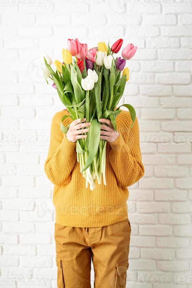 Happy beautiful woman in yellow clothes holding bouquet of tulips photo