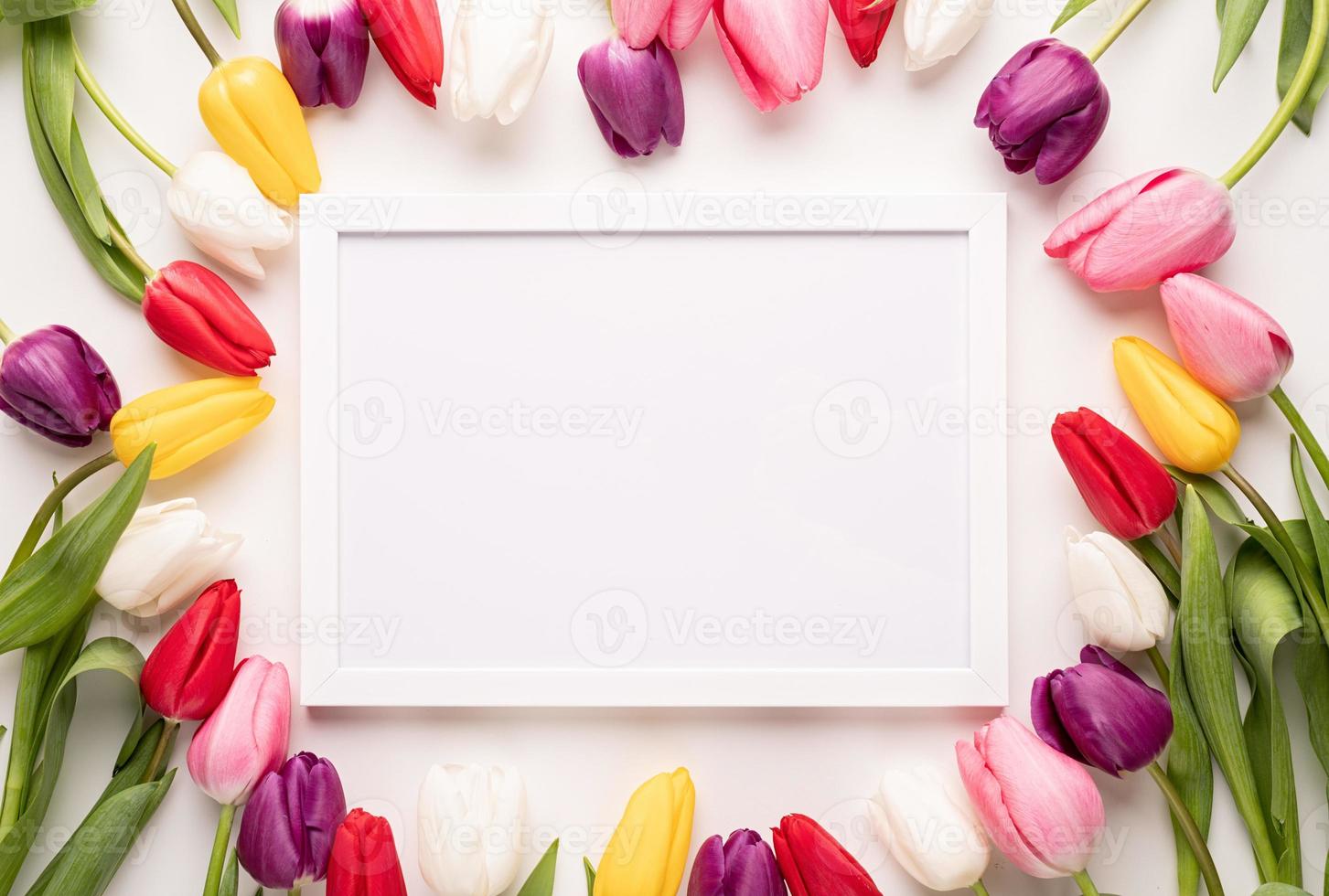 White frame with colorful spring tulips top view over white background photo