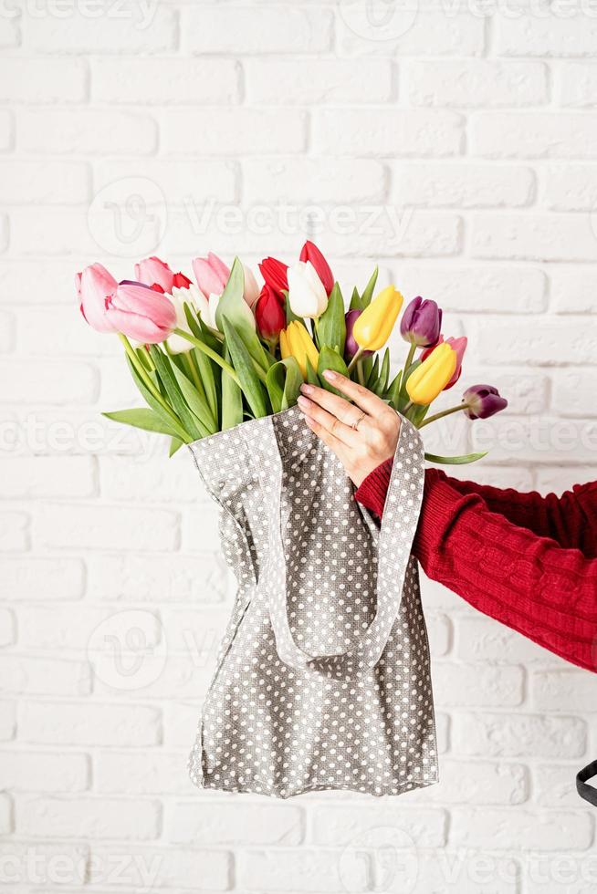 Mano de mujer sosteniendo una bolsa de tela de lunares grises con coloridos tulipanes foto