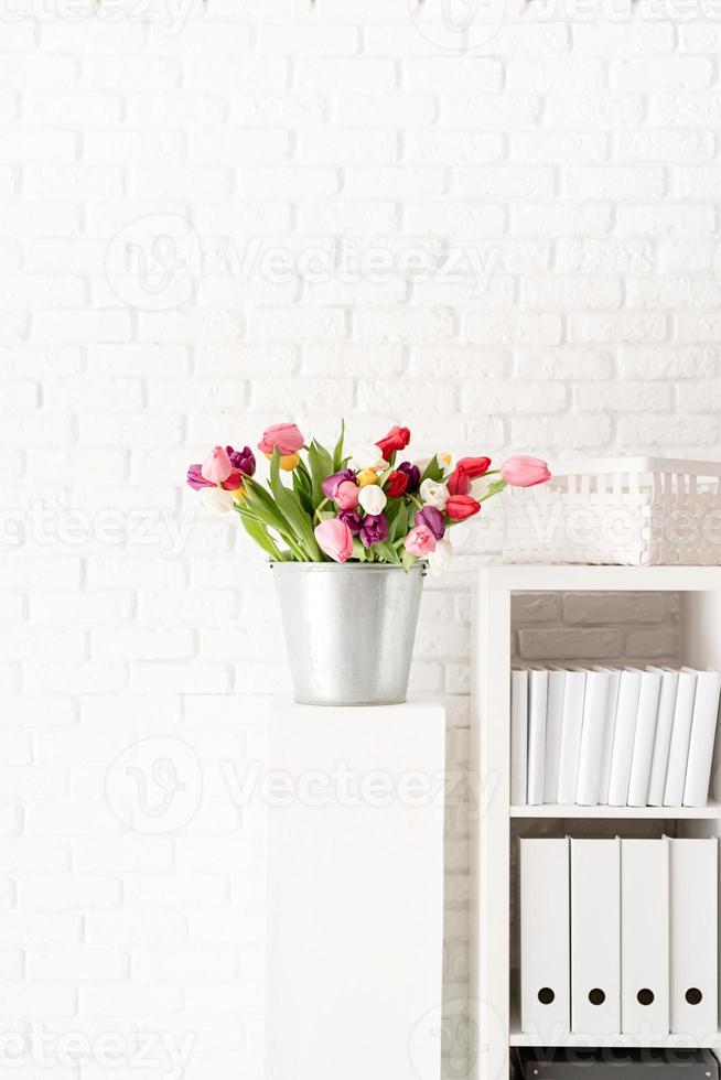 Bucket of tulip flowers next to the bookshelf photo