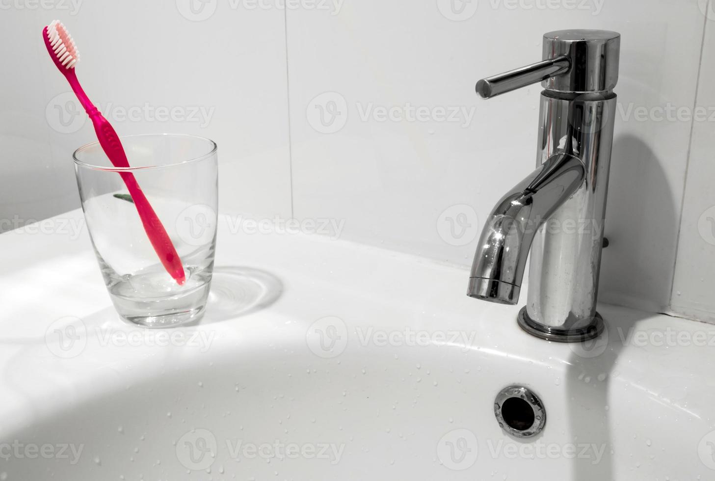 grifo del baño y lavabo con vaso de agua y cepillo de dientes foto