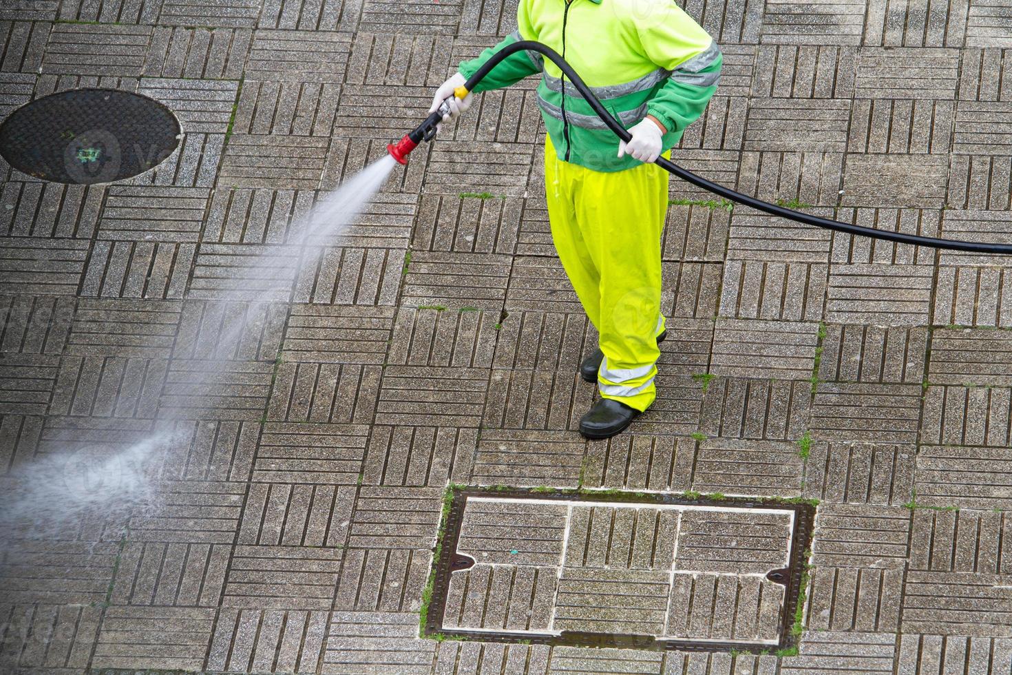 Worker holding a hose cleaning a sidewalk with water photo
