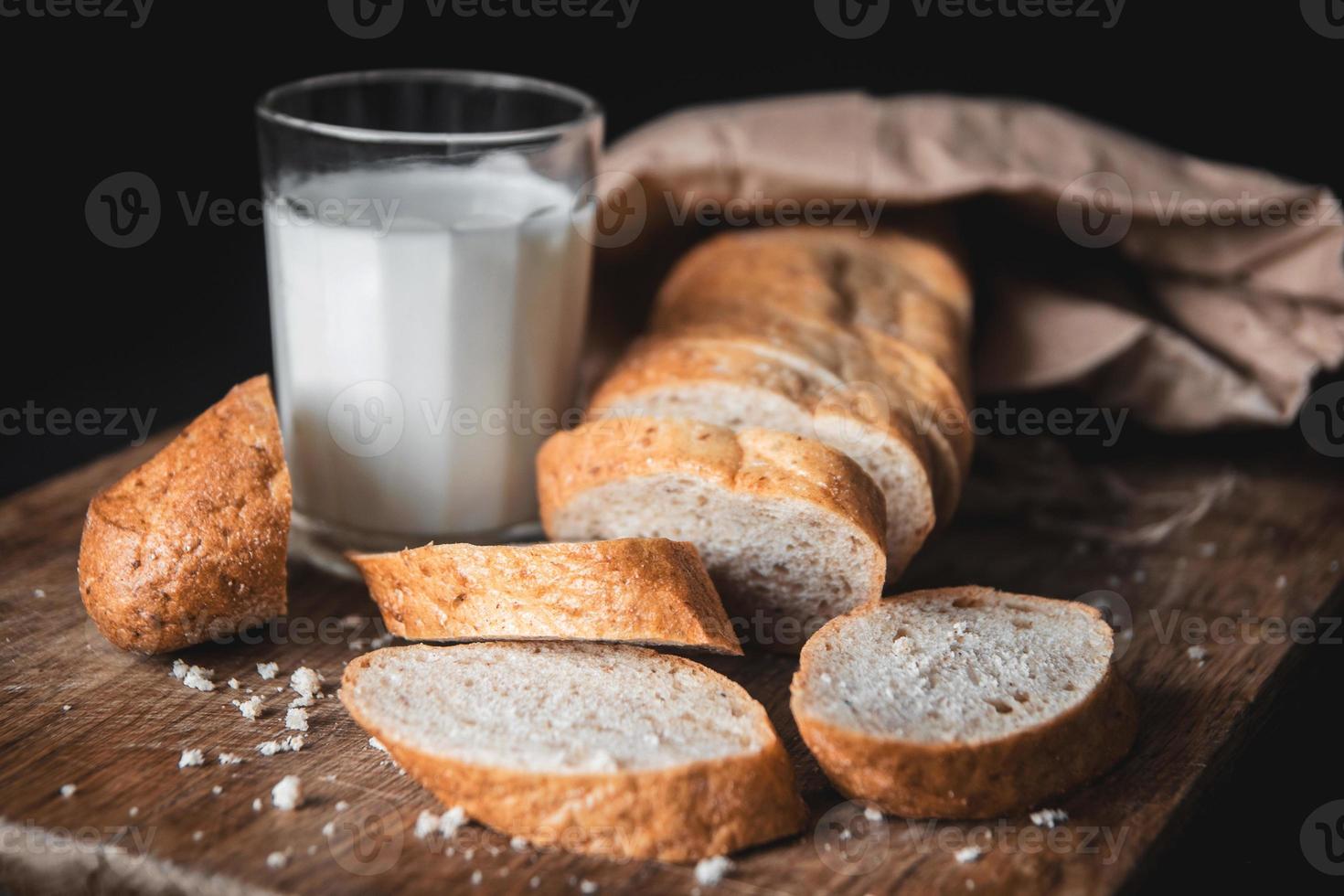 Bread with cut pieces lie on a wooden board and a glass of fresh milk photo