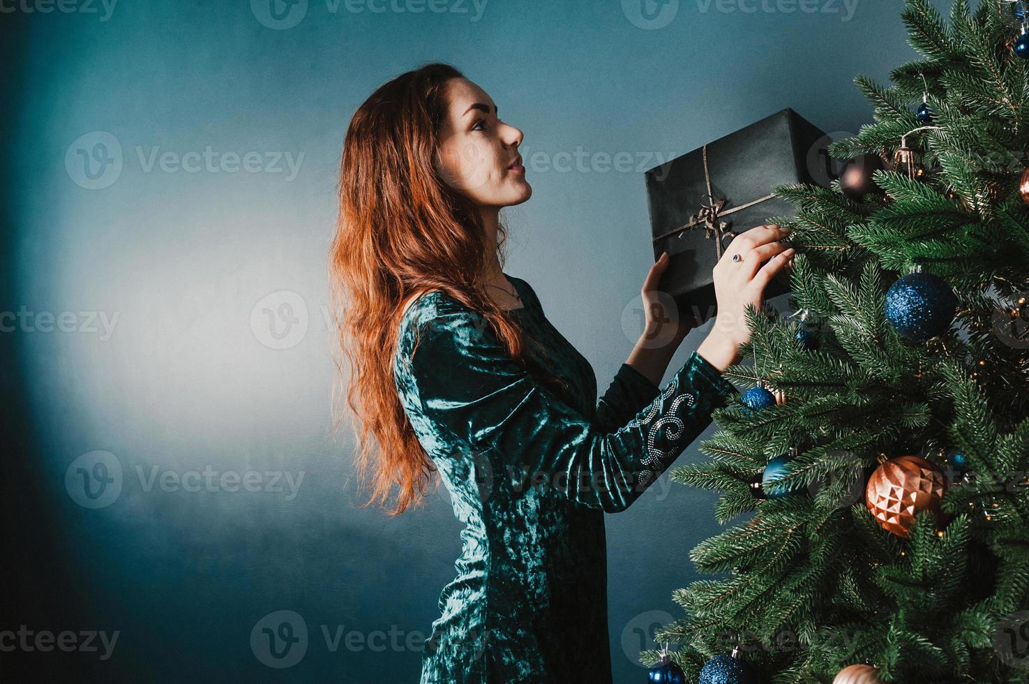 Beautiful woman decorating Christmas tree holding a gift box photo