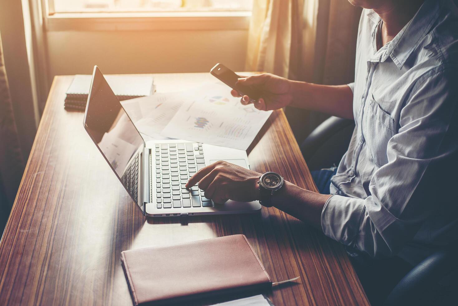 Businessman hands using cell phone with laptop at office desk. photo