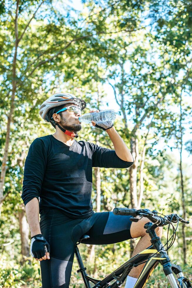 los ciclistas se paran en la cima de la montaña y beben una botella de agua. foto