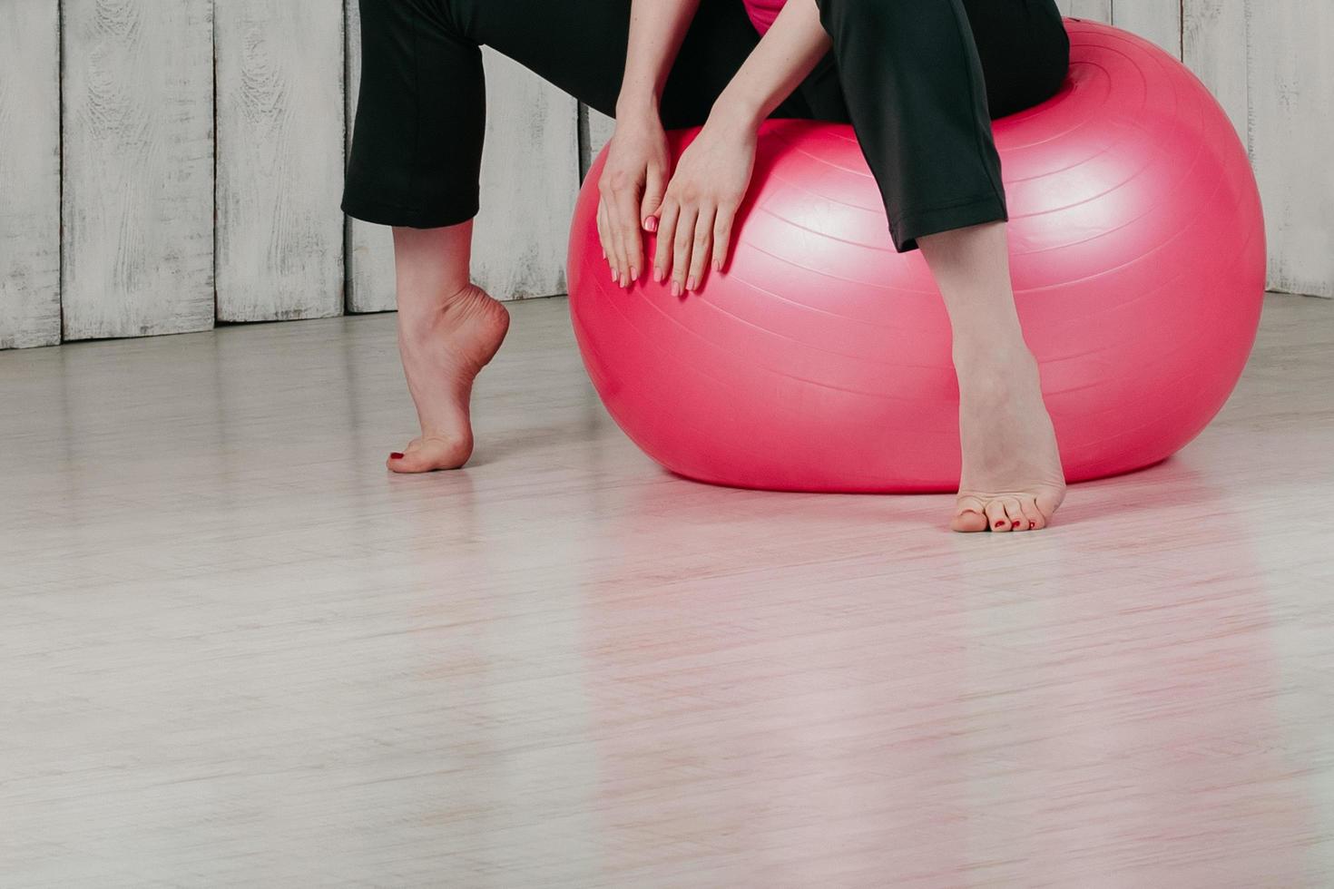 Una niña sentada sobre una pelota rosa en forma en un gimnasio, fondo claro foto