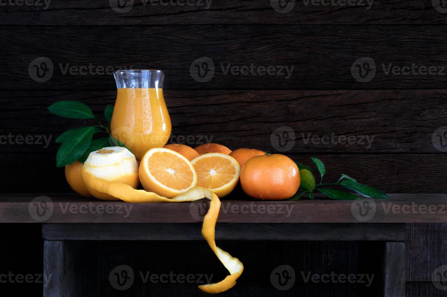 Naranjas frescas con hojas y jugo de naranja en vidrio sobre mesa de madera foto
