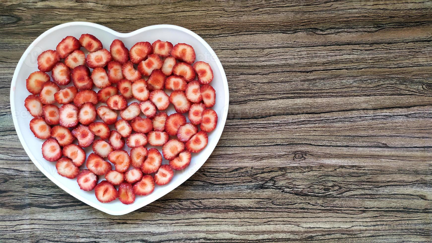 las fresas en rodajas están en un plato en forma de corazón. servicio romántico foto