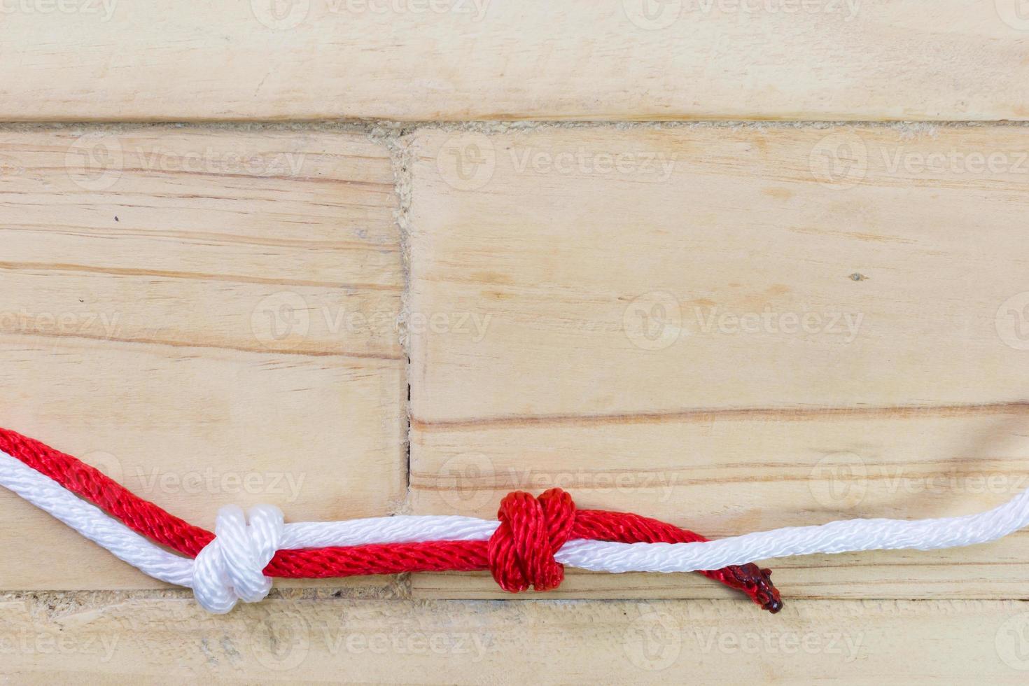 nudo de pescador hecho con cuerda roja sobre fondo de madera. foto