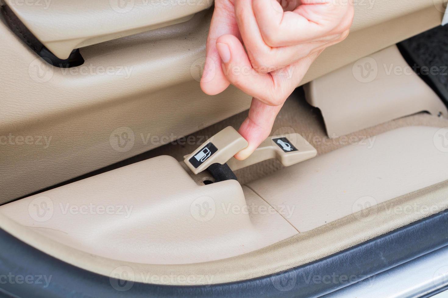 closeup hand pulling fuel door open button in a car photo