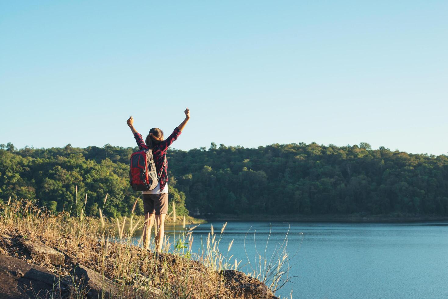 Young woman hiker open arms at mountain peak, Below her is big lake. photo