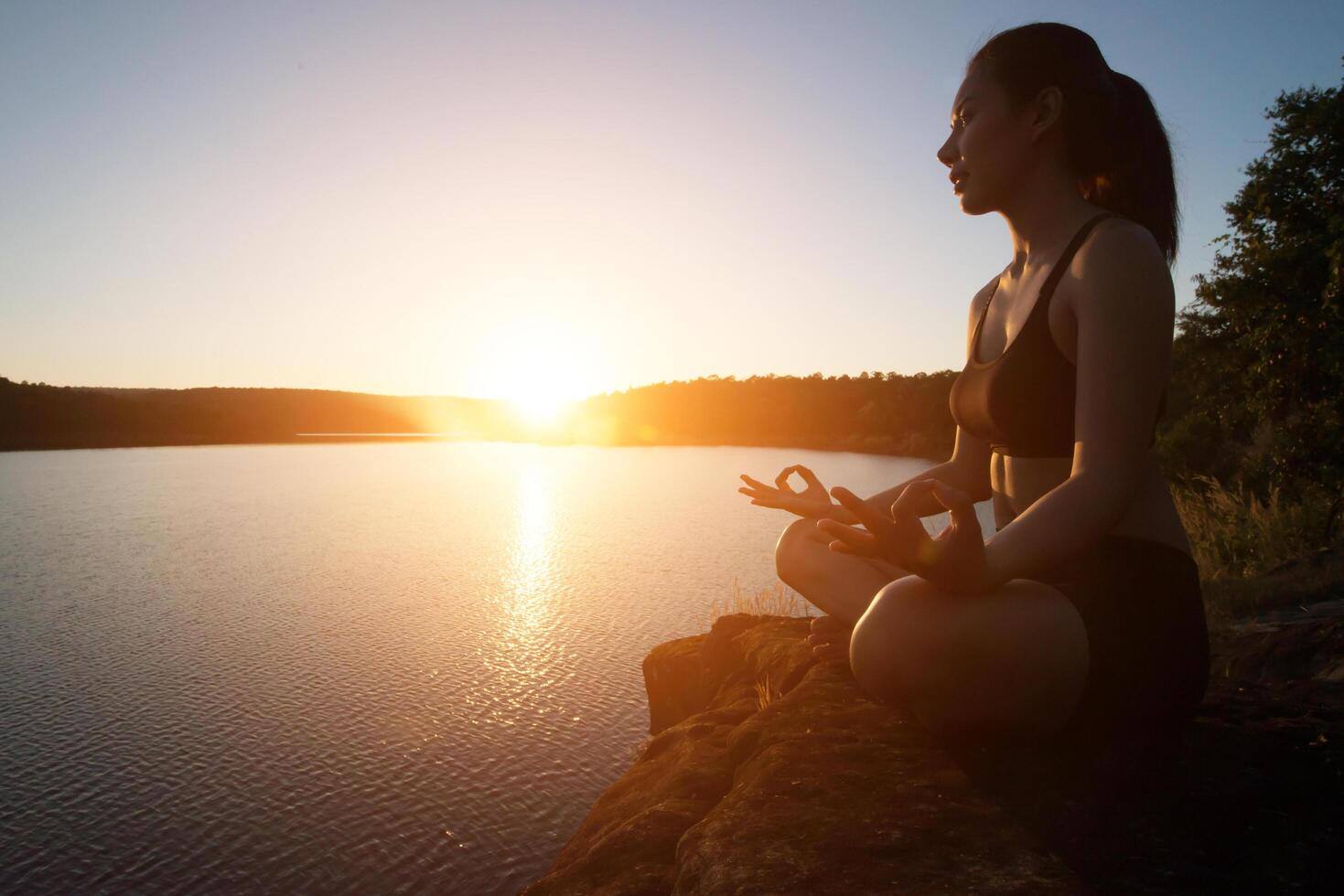 joven sana está practicando yoga en el lago de la montaña durante la puesta de sol. foto