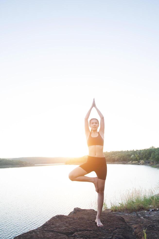 Young healthy woman is practicing yoga at mountain lake during sunset. photo