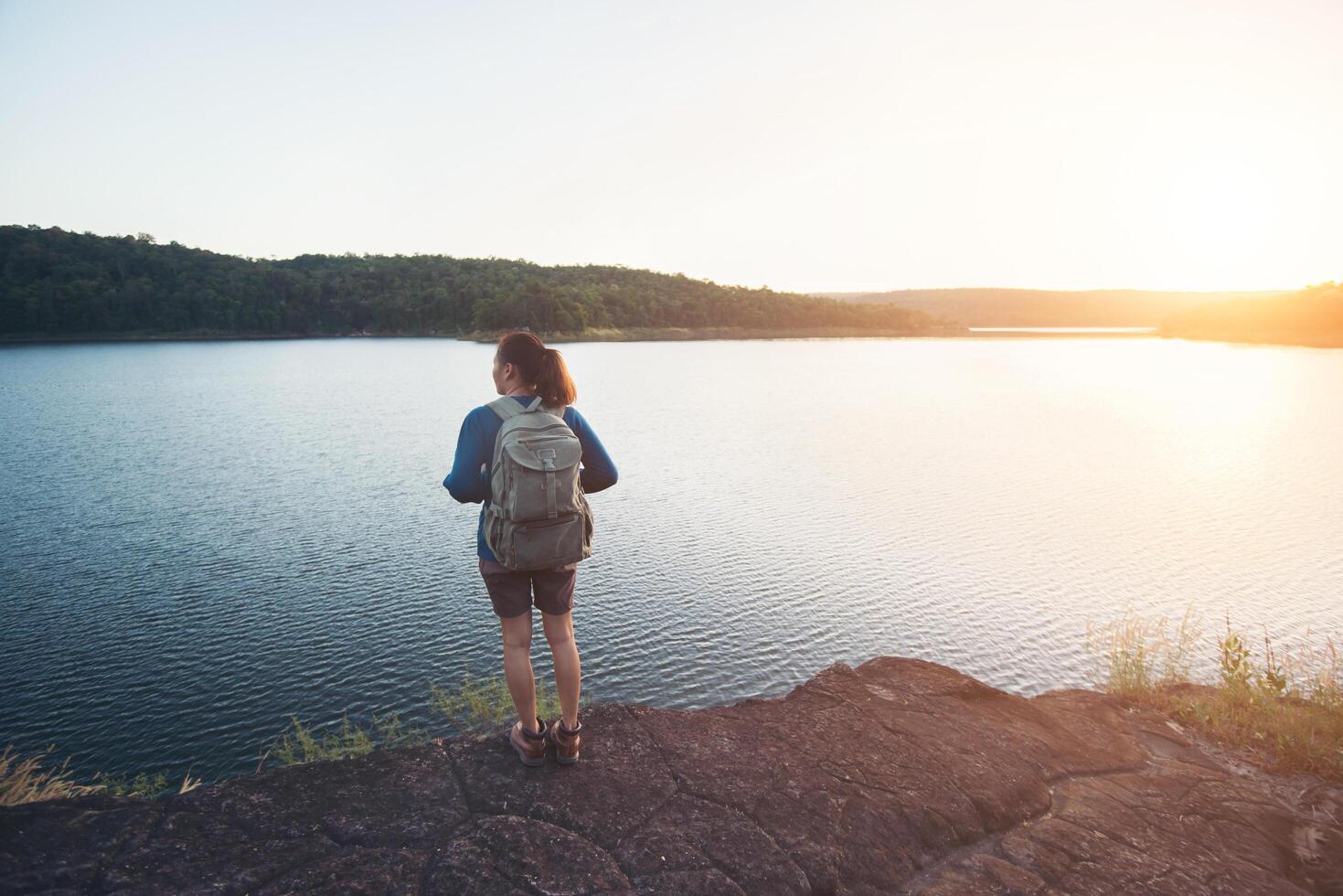 mujer joven excursionista de pie sobre la roca y disfrutar de la puesta de sol sobre el lago. foto