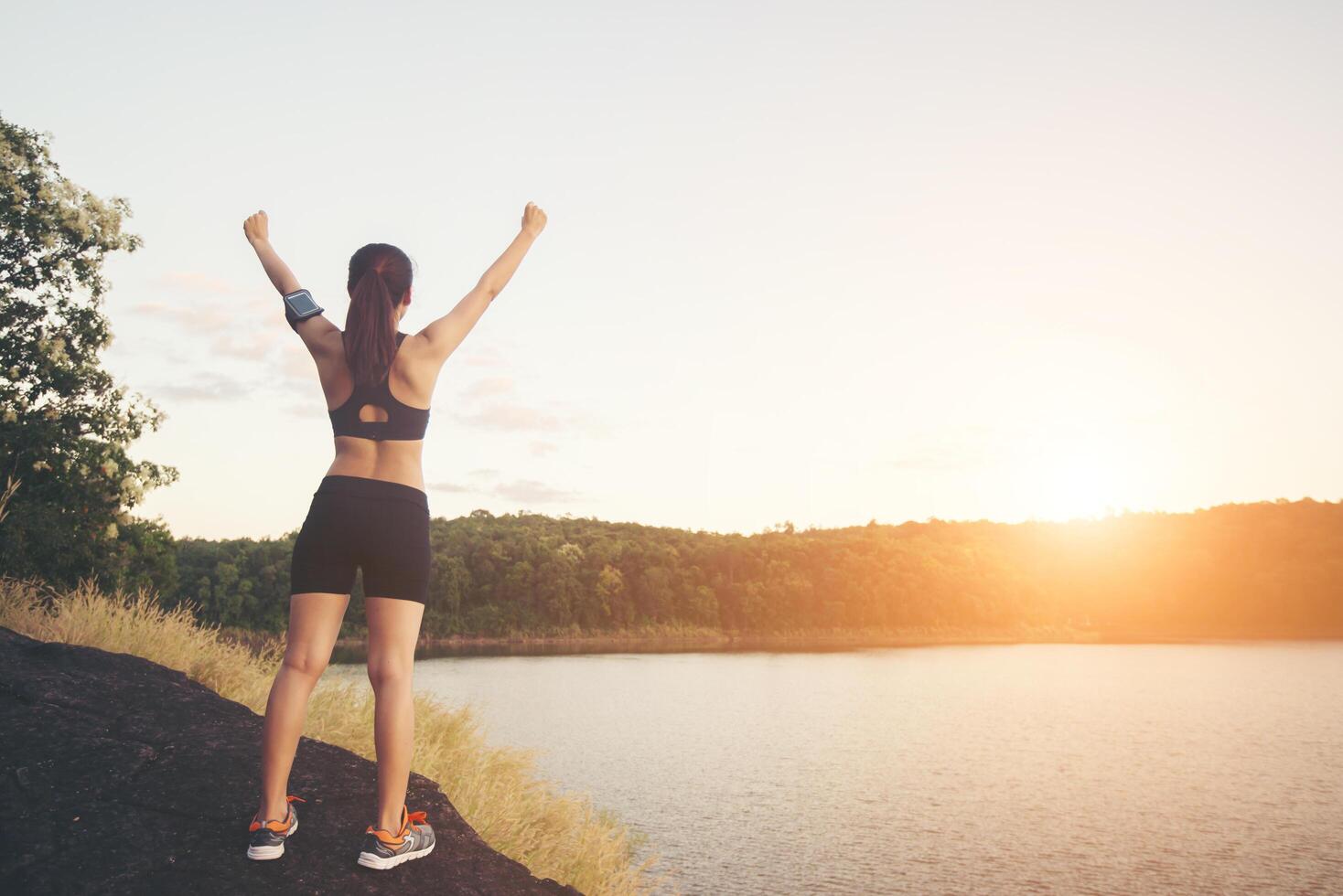 mujer joven fitness lograr senderismo en la cima con vista al lago al atardecer. foto