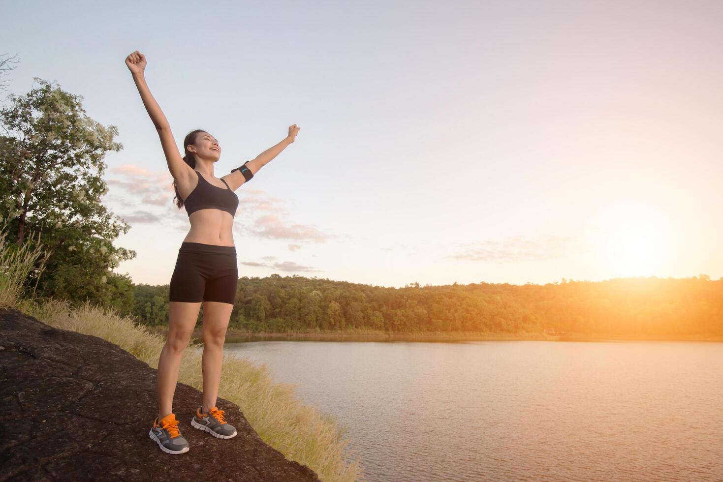 mujer joven fitness lograr senderismo en la cima con vista al lago al atardecer. foto