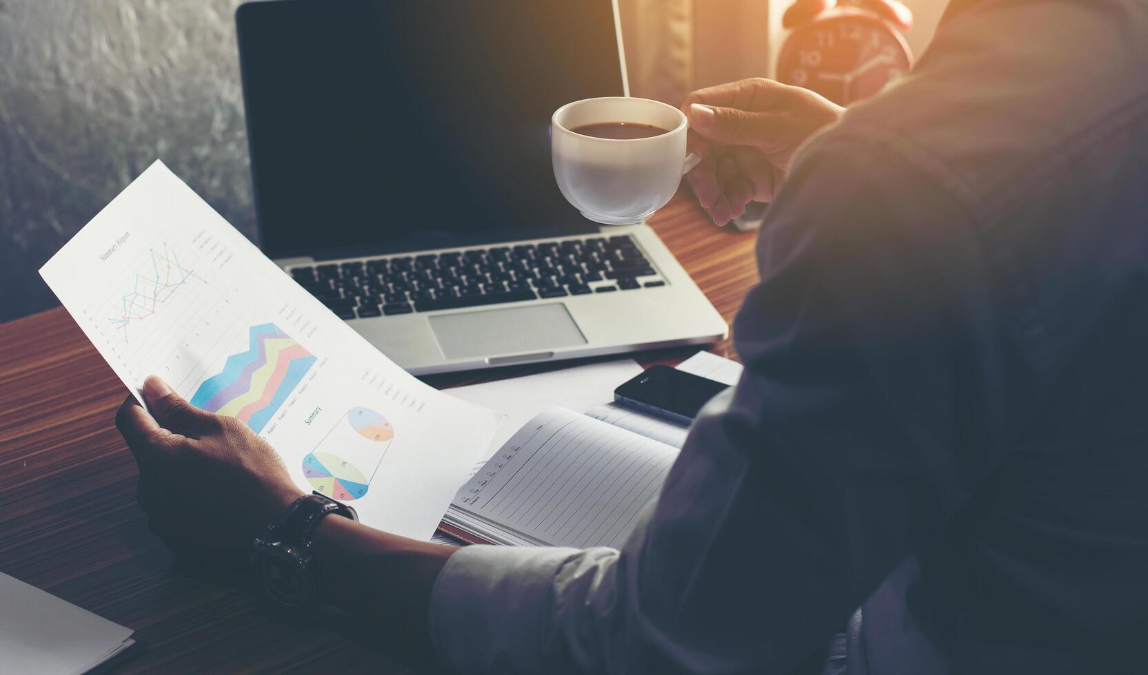 gráfico financiero de análisis de empresario y sosteniendo una taza de café. foto