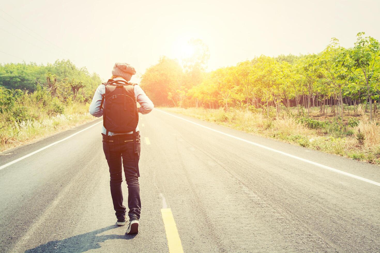 mujer joven haciendo autostop con mochila caminando por la carretera. foto