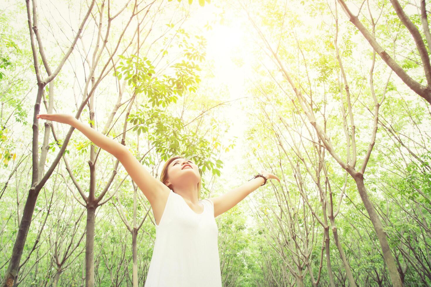 Young beautiful woman raised arms enjoying the fresh in green forest. photo