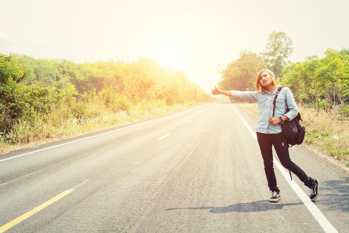 Mujer joven inconformista haciendo autostop en la carretera rural esperar el coche foto