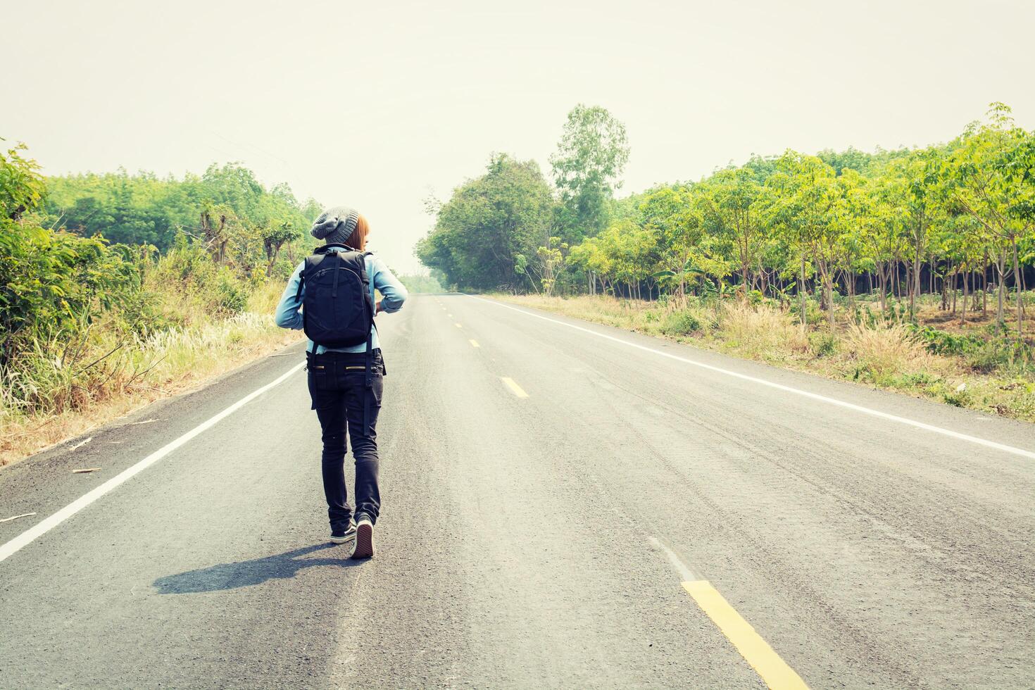 mujer joven haciendo autostop con mochila caminando por la carretera. foto