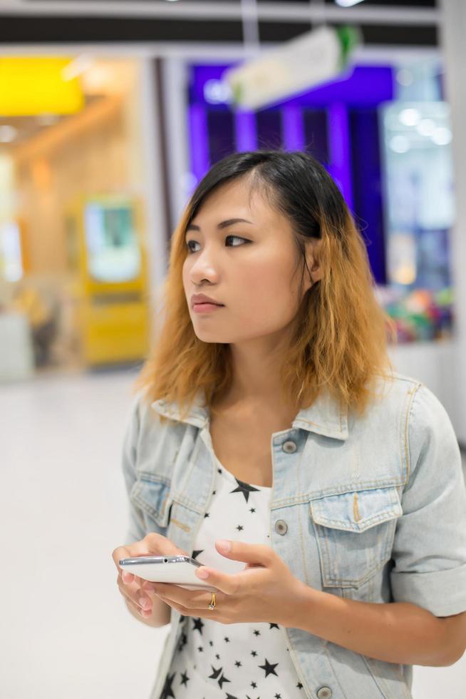 mujer joven enviando mensajes de texto en el teléfono inteligente caminando en el centro comercial. foto