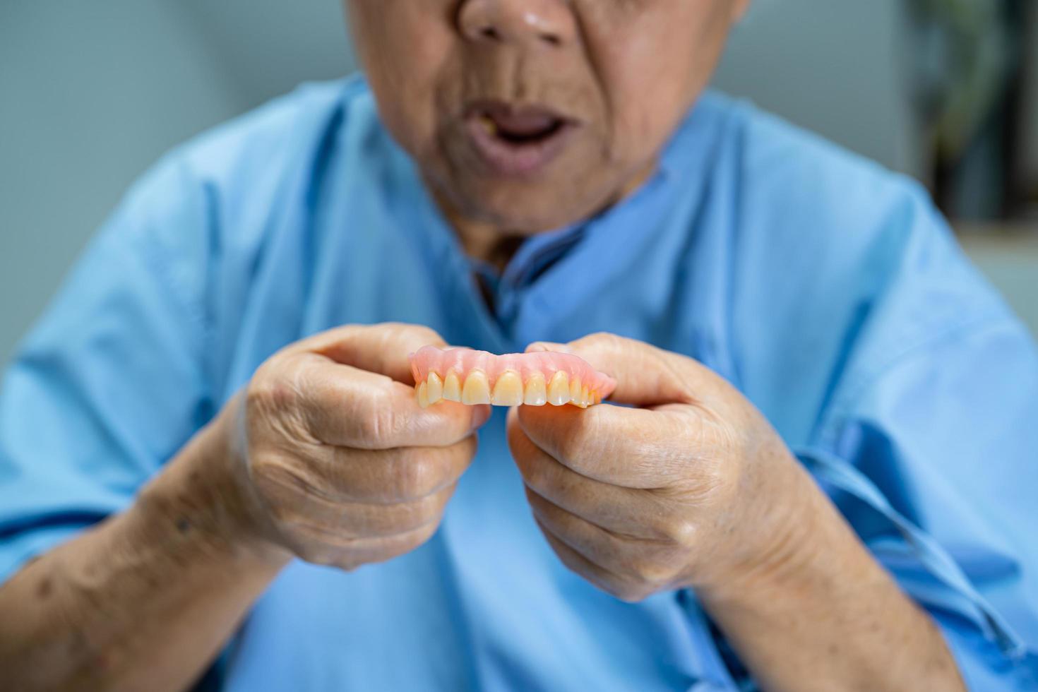 Paciente asiático mayor o anciano sosteniendo para usar dentadura en la sala del hospital de enfermería, concepto médico fuerte y saludable foto