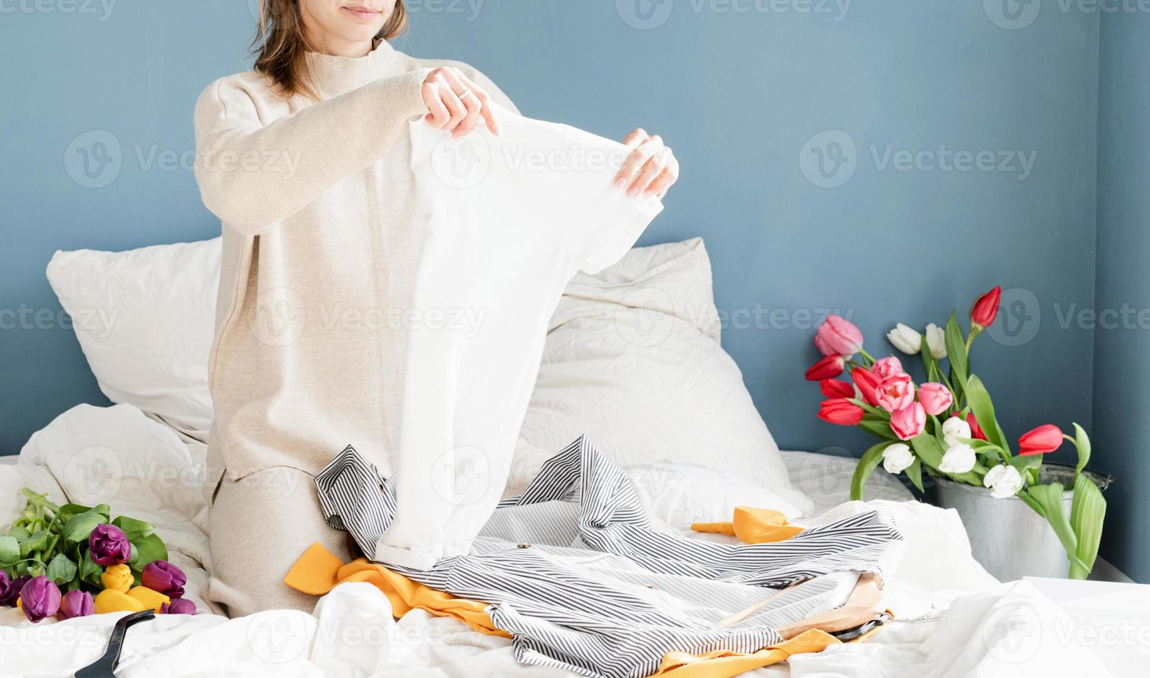 Mujer joven organizando ropa sentada en la cama en casa foto