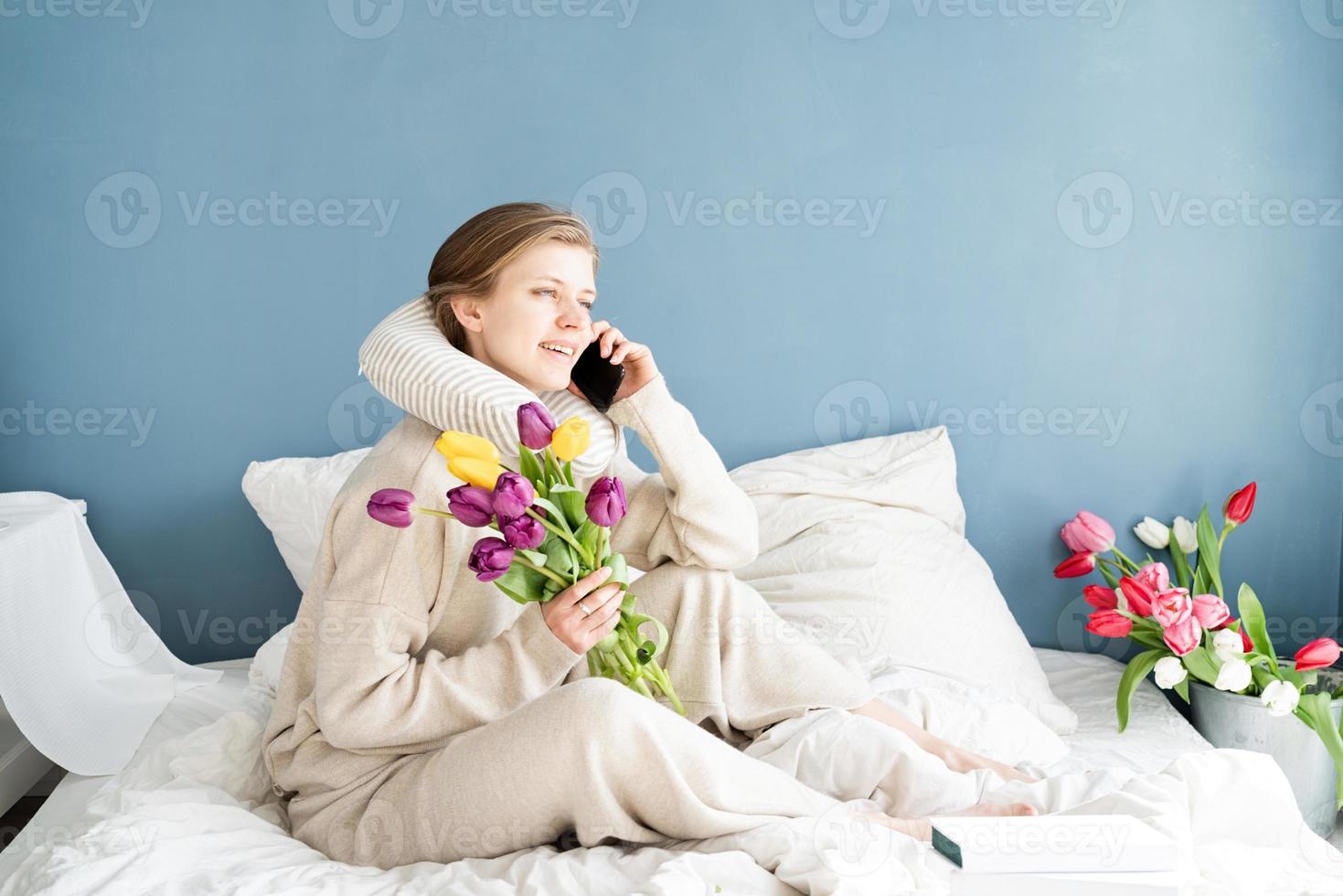 woman sitting on the bed wearing pajamas talking on the phone photo