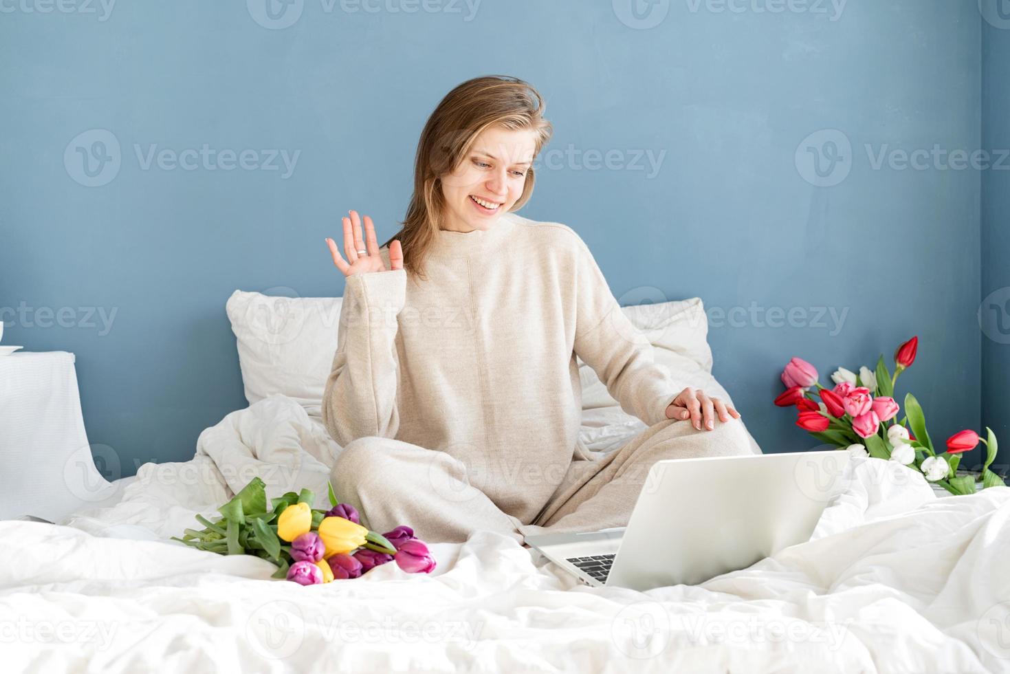 woman sitting on the bed wearing pajamas chatting on laptop photo
