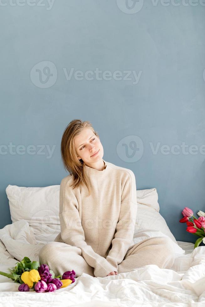 woman sitting on the bed holding tulip flowers bouquet photo