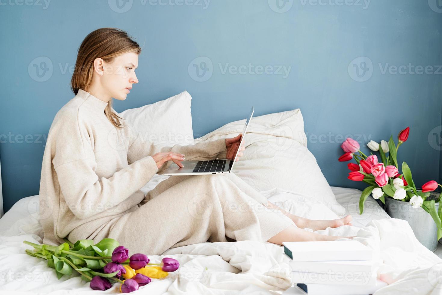 Mujer sentada en la cama vistiendo pijama bouquet charlando en el portátil foto